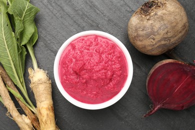 Photo of Tasty horseradish sauce with beetroot, roots and vegetable on black table, flat lay