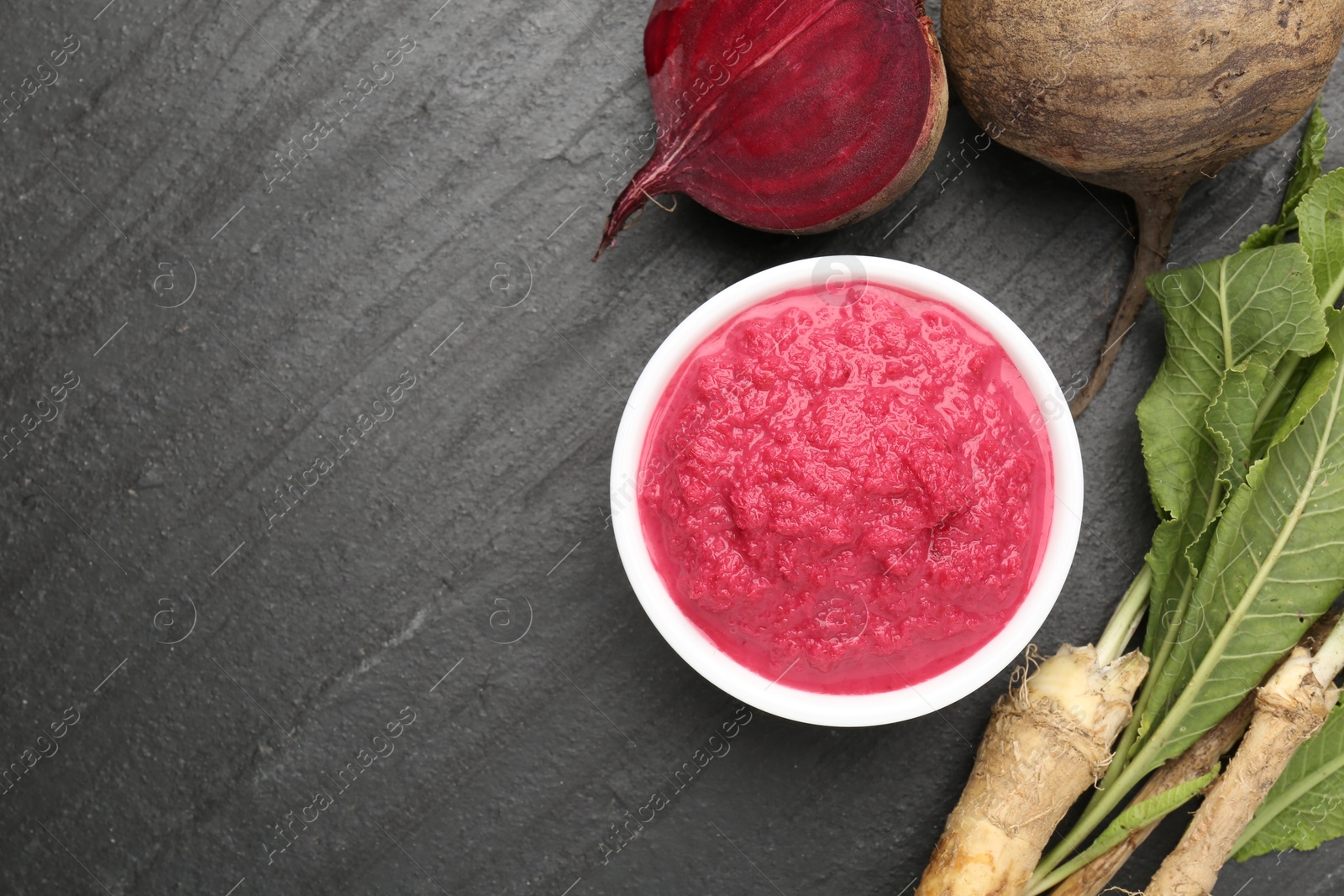 Photo of Tasty horseradish sauce with beetroot, roots and vegetable on black table, flat lay. Space for text