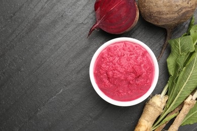 Photo of Tasty horseradish sauce with beetroot, roots and vegetable on black table, flat lay. Space for text