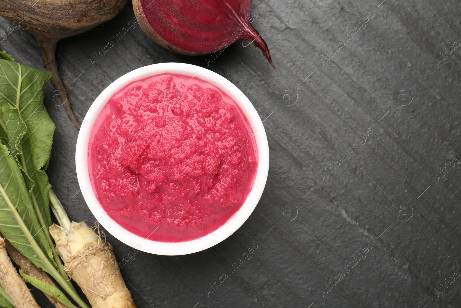 Photo of Tasty horseradish sauce with beetroot, roots and vegetable on black table, flat lay. Space for text