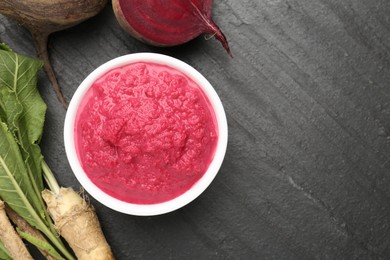 Photo of Tasty horseradish sauce with beetroot, roots and vegetable on black table, flat lay. Space for text