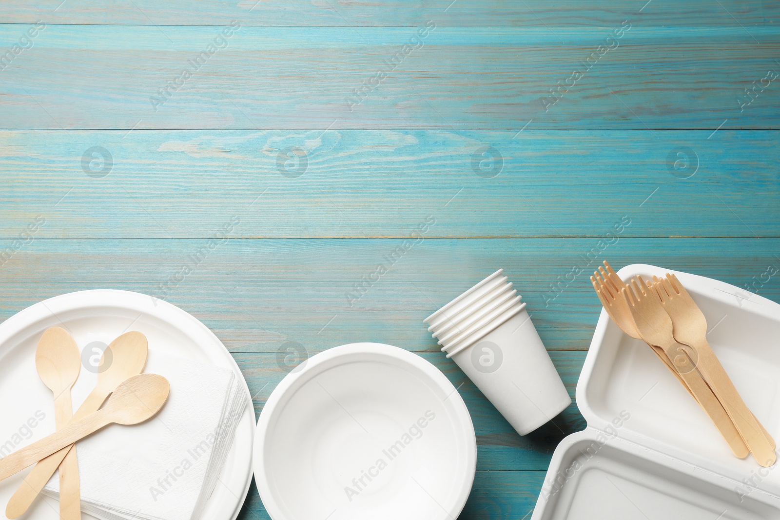Photo of Set of disposable tableware on light blue wooden table, flat lay. Space for text