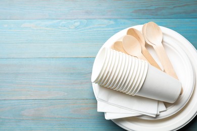 Photo of Set of disposable tableware and napkins on light blue wooden table, top view. Space for text