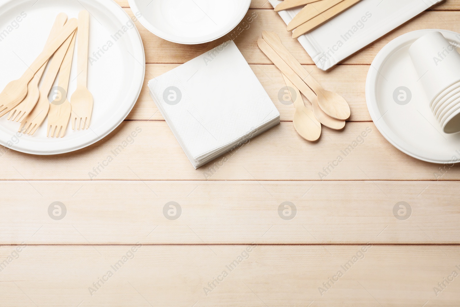 Photo of Set of disposable tableware and napkins on wooden table, flat lay. Space for text