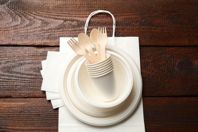 Photo of Set of disposable tableware, paper bag and napkins on wooden table, top view