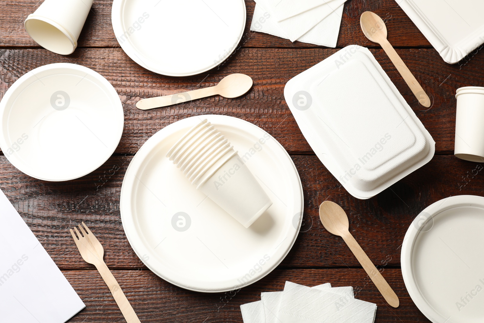 Photo of Set of disposable tableware and napkins on wooden table, flat lay