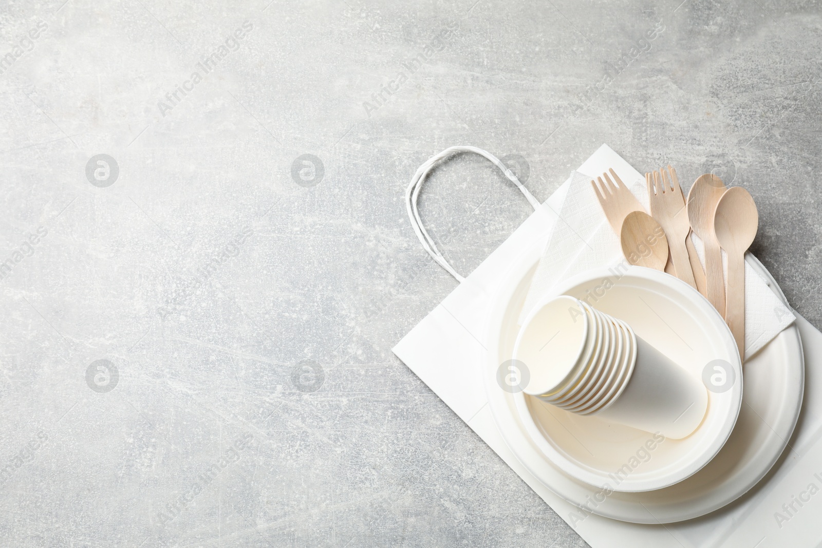 Photo of Set of disposable tableware, paper bag and napkins on grey table, top view. Space for text