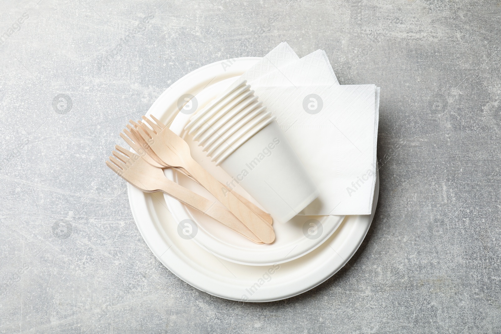 Photo of Set of disposable tableware and napkins on grey table, top view
