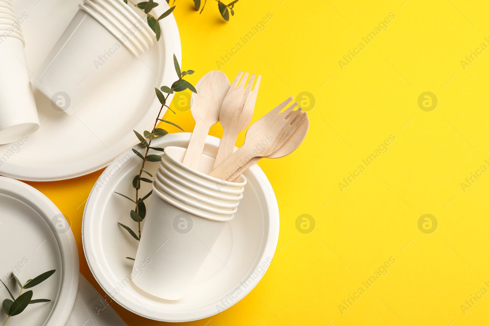 Photo of Disposable tableware and eucalyptus branches on yellow background, above view. Space for text