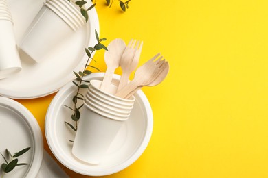 Photo of Disposable tableware and eucalyptus branches on yellow background, above view. Space for text
