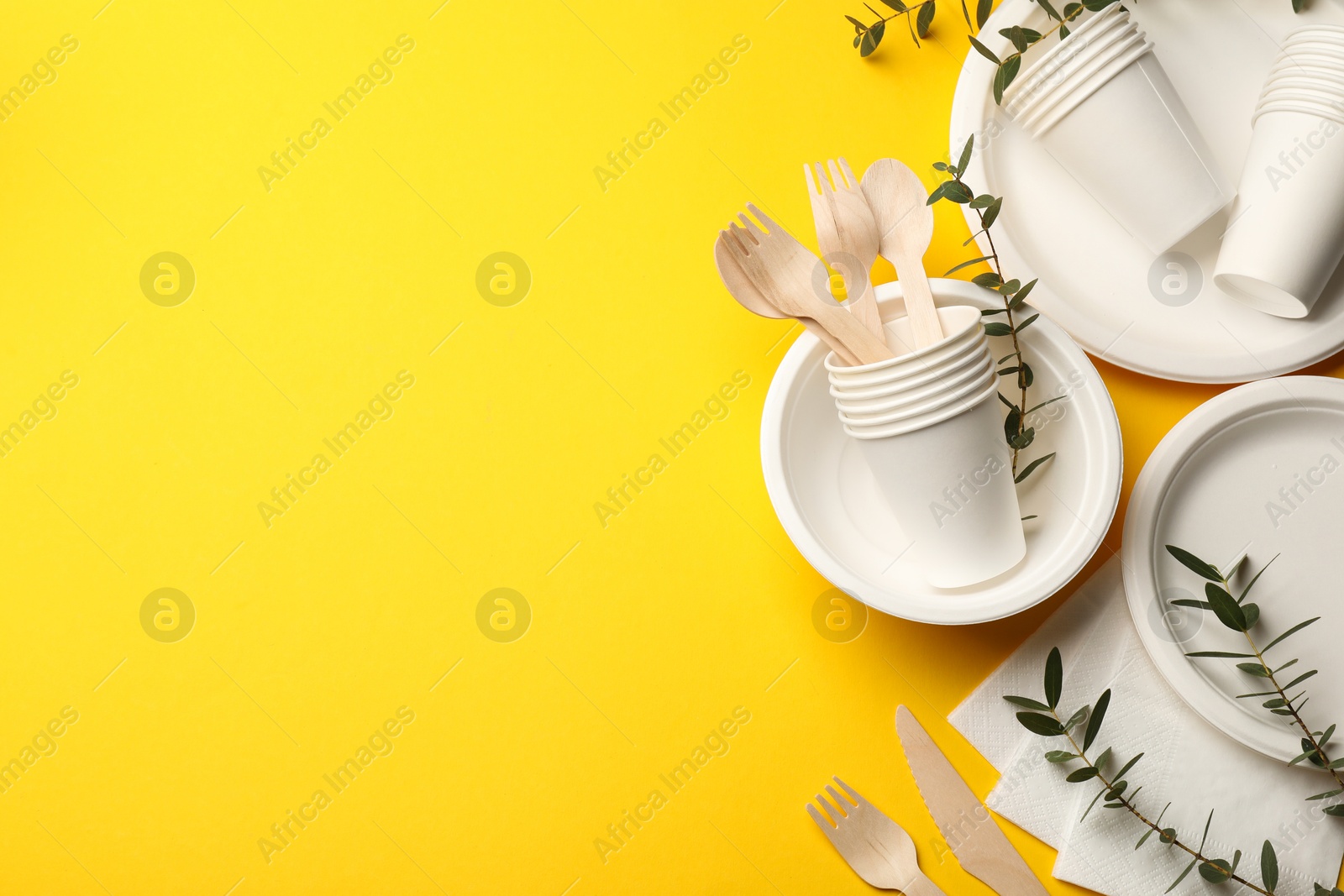Photo of Disposable tableware and eucalyptus branches on yellow background, flat lay. Space for text