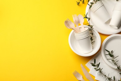 Photo of Disposable tableware and eucalyptus branches on yellow background, flat lay. Space for text