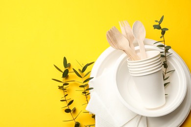 Photo of Disposable tableware and eucalyptus branches on yellow background, above view. Space for text
