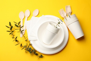 Photo of Disposable tableware and eucalyptus branches on yellow background, flat lay