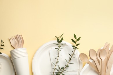 Photo of Disposable tableware and eucalyptus branches on beige background, flat lay. Space for text