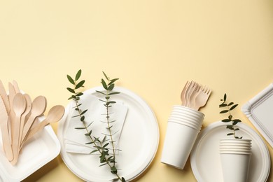 Photo of Disposable tableware and eucalyptus branches on beige background, flat lay. Space for text