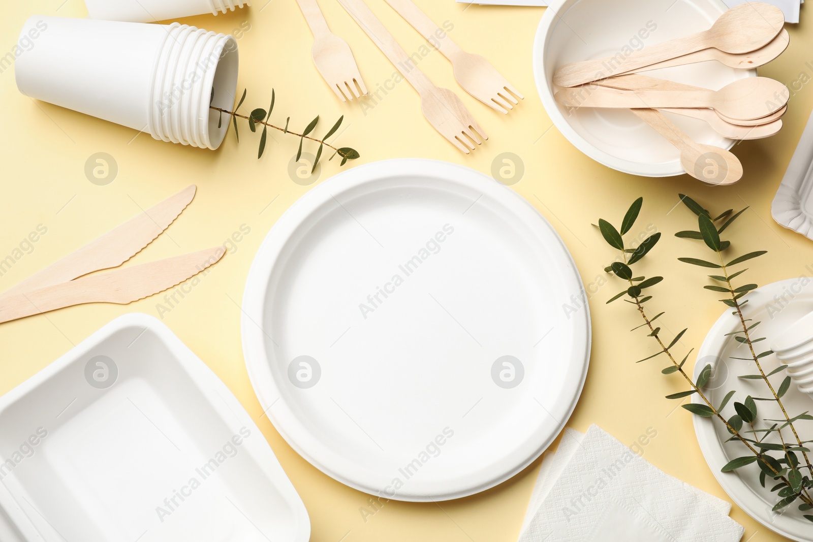 Photo of Disposable tableware and eucalyptus branches on beige background, flat lay
