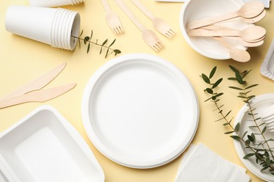 Photo of Disposable tableware and eucalyptus branches on beige background, flat lay