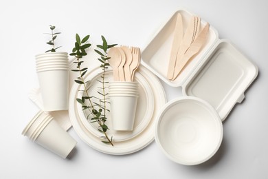 Photo of Disposable tableware and eucalyptus branches on light background, flat lay