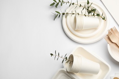 Photo of Disposable tableware and eucalyptus branches on light background, flat lay. Space for text