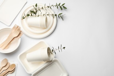 Photo of Disposable tableware and eucalyptus branches on light background, flat lay. Space for text
