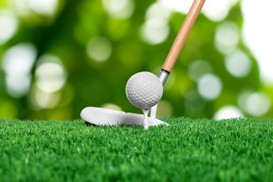 Image of Golf ball, tee, club and green grass against blurred background