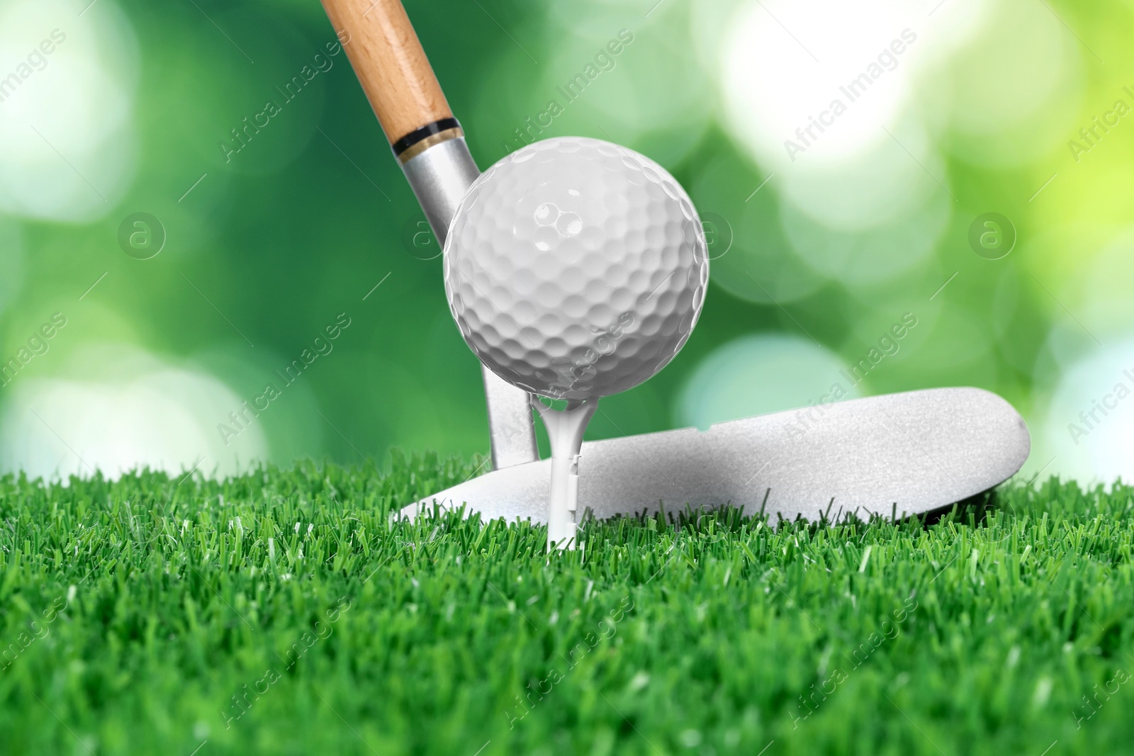 Image of Golf ball, tee, club and green grass against blurred background
