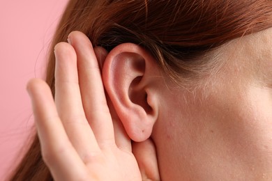 Photo of Sound. Woman showing hand to ear gesture on pink background, closeup
