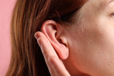 Photo of Sound. Woman showing hand to ear gesture on pink background, closeup