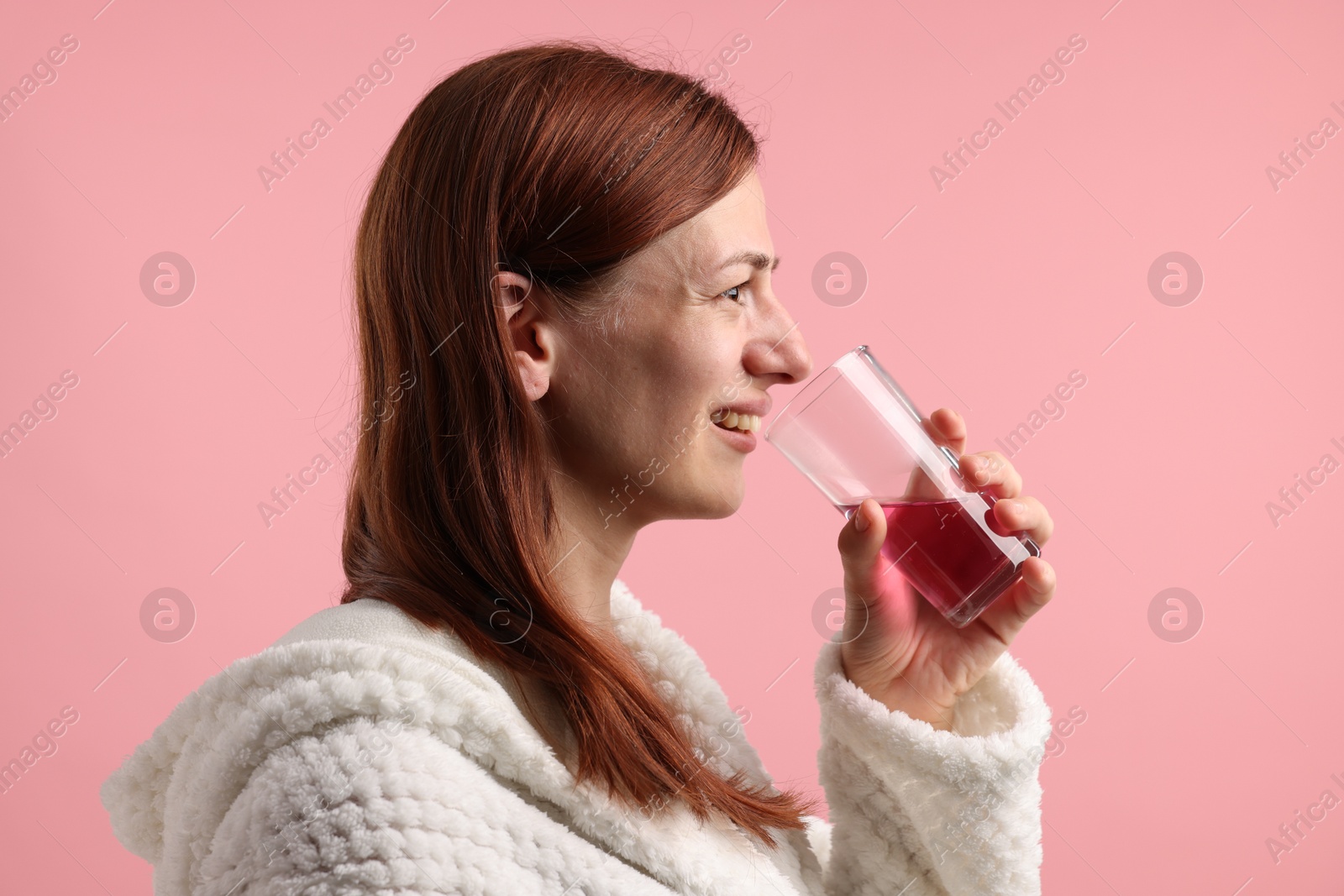 Photo of Woman rinsing mouth with mouthwash on pink background