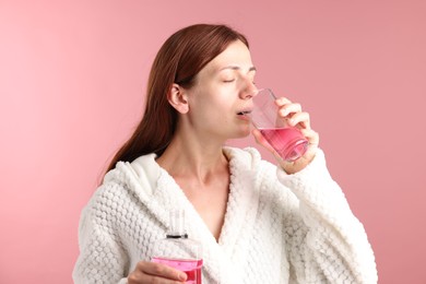 Photo of Woman rinsing mouth with mouthwash on pink background