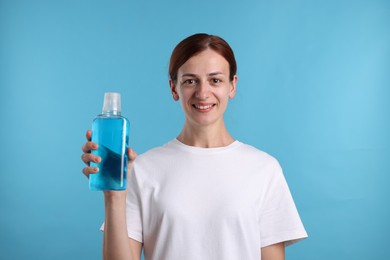 Photo of Woman rinsing mouth with mouthwash on light blue background