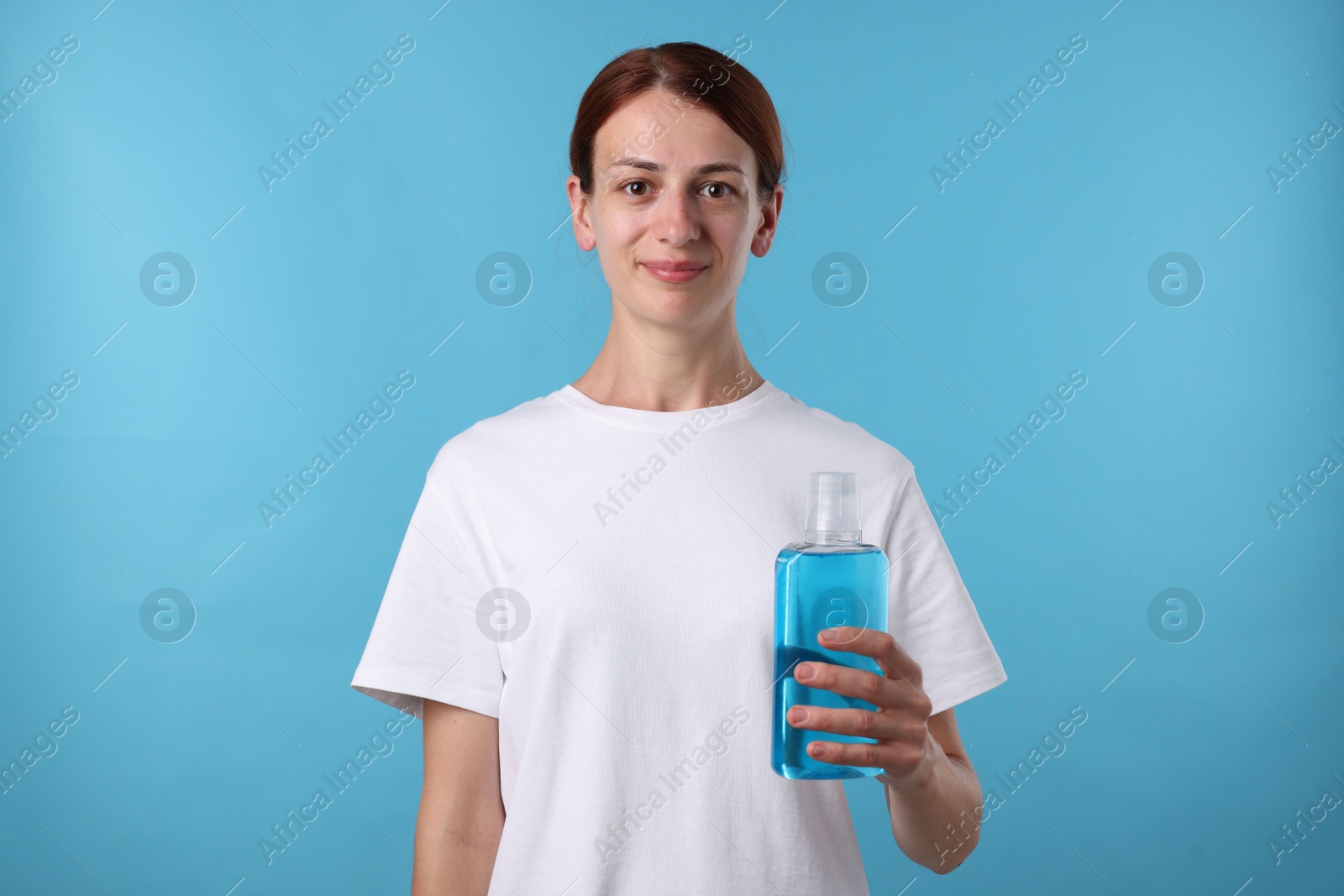 Photo of Woman rinsing mouth with mouthwash on light blue background
