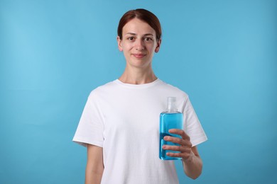 Photo of Woman rinsing mouth with mouthwash on light blue background
