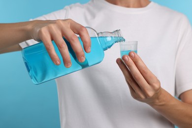 Photo of Woman rinsing mouth with mouthwash on light blue background, closeup