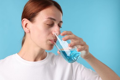 Photo of Woman rinsing mouth with mouthwash on light blue background
