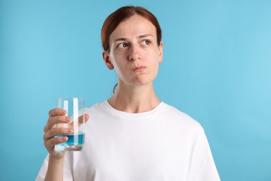 Photo of Woman rinsing mouth with mouthwash on light blue background