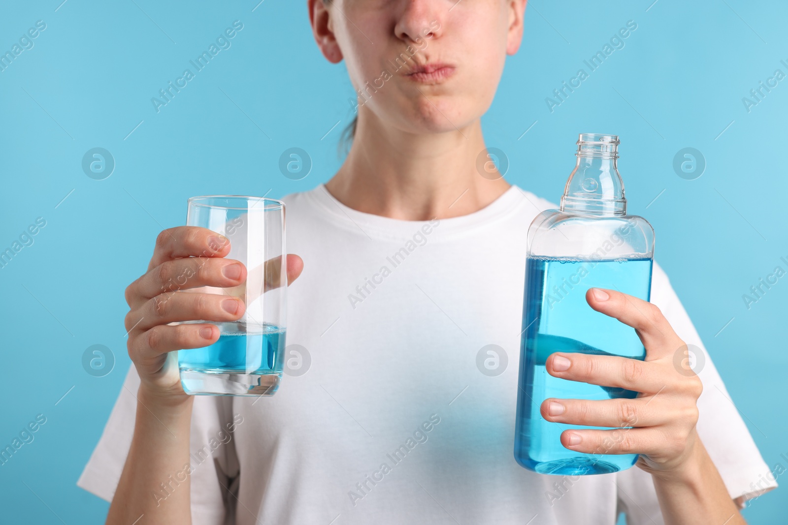 Photo of Woman rinsing mouth with mouthwash on light blue background, closeup
