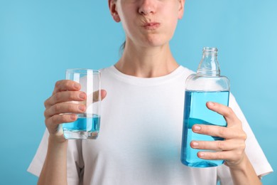 Photo of Woman rinsing mouth with mouthwash on light blue background, closeup