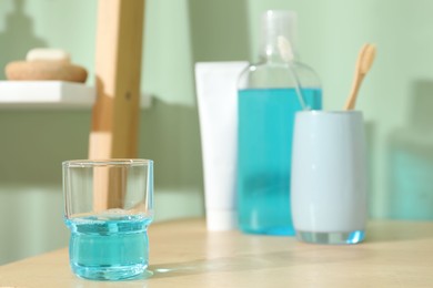Photo of Glass of mouthwash on wooden shelf in bathroom