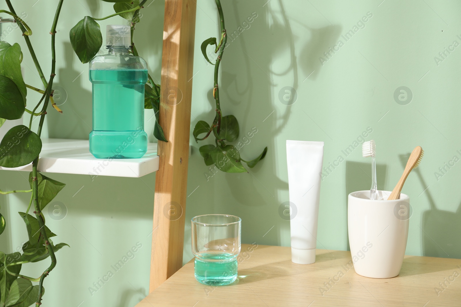 Photo of Glass of mouthwash, toothbrushes and toothpaste on shelf in bathroom