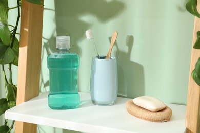 Photo of Bottle of mouthwash, toothbrushes and soap on shelf in bathroom