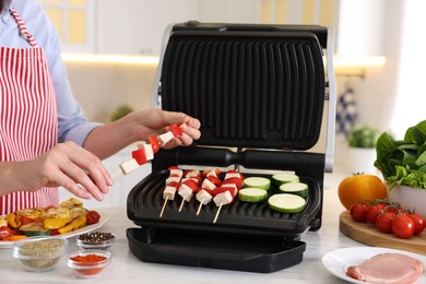 Photo of Woman cooking skewers with meat and vegetables on electric grill at home, closeup