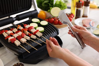 Photo of Woman cooking skewers with meat and vegetables on electric grill at home, closeup