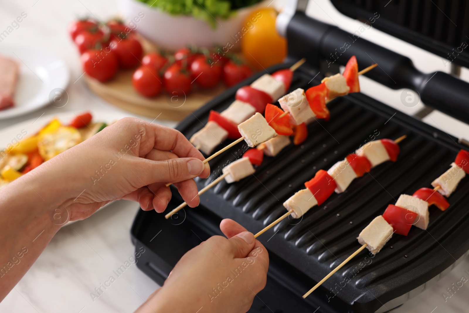 Photo of Woman cooking skewers with meat and vegetables on electric grill at home, closeup