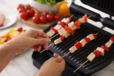 Photo of Woman cooking skewers with meat and vegetables on electric grill at home, closeup