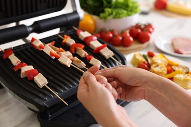 Photo of Woman cooking skewers with meat and vegetables on electric grill at home, closeup