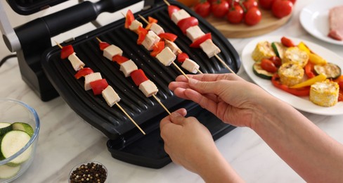 Photo of Woman cooking skewers with meat and vegetables on electric grill at home, closeup