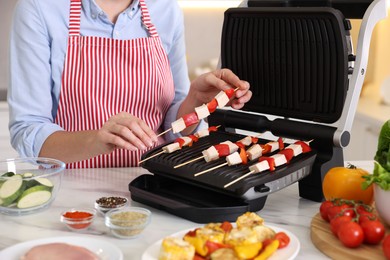 Photo of Woman cooking skewers with meat and vegetables on electric grill at home, closeup