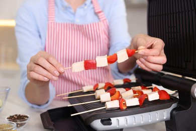 Photo of Woman cooking skewers with meat and vegetables on electric grill at home, closeup